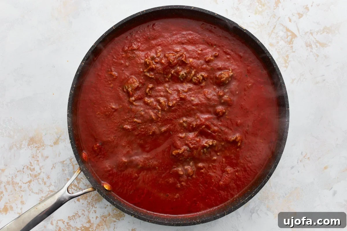 Irresistible Gluten-Free Lasagna 6 Gluten-free pasta sauce being stirred into cooked ground beef in a black skillet, creating a rich meat sauce.