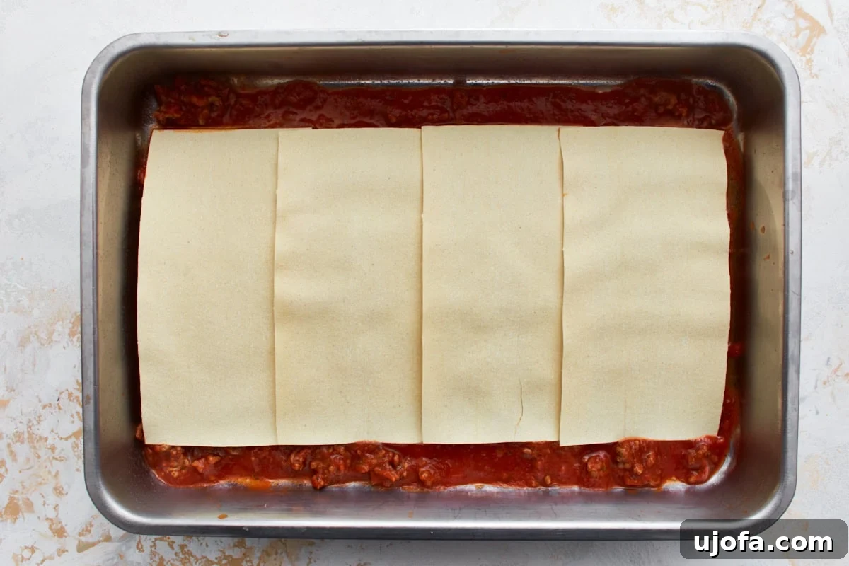 Irresistible Gluten-Free Lasagna 9 First layer of gluten-free lasagna with meat sauce covering the bottom of a tin baking dish, topped with four Barilla gluten-free lasagna sheets.