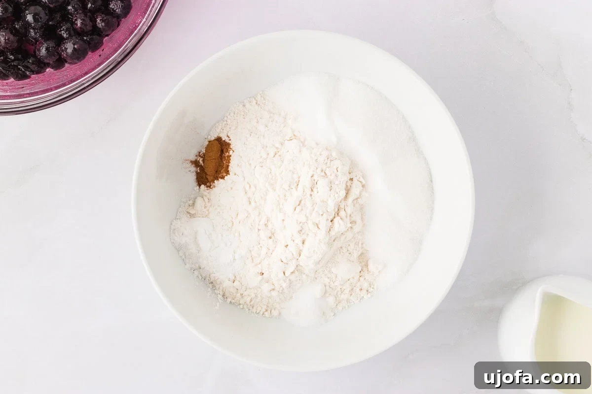 Gluten-free flour, sugar, baking powder, cinnamon, and salt mixed in a white bowl with a pitcher of milk nearby.