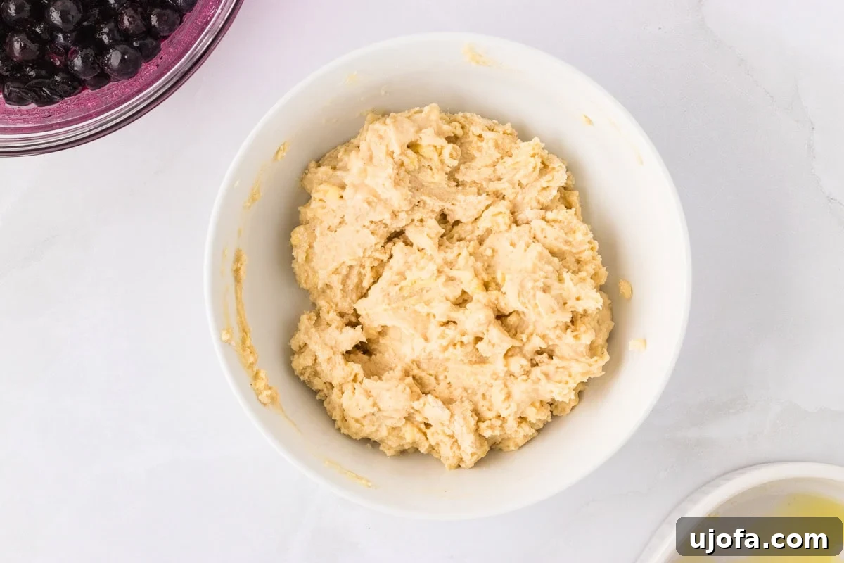 Shaggy, thick gluten-free biscuit dough in a white bowl, ready to be scooped onto blueberry filling.