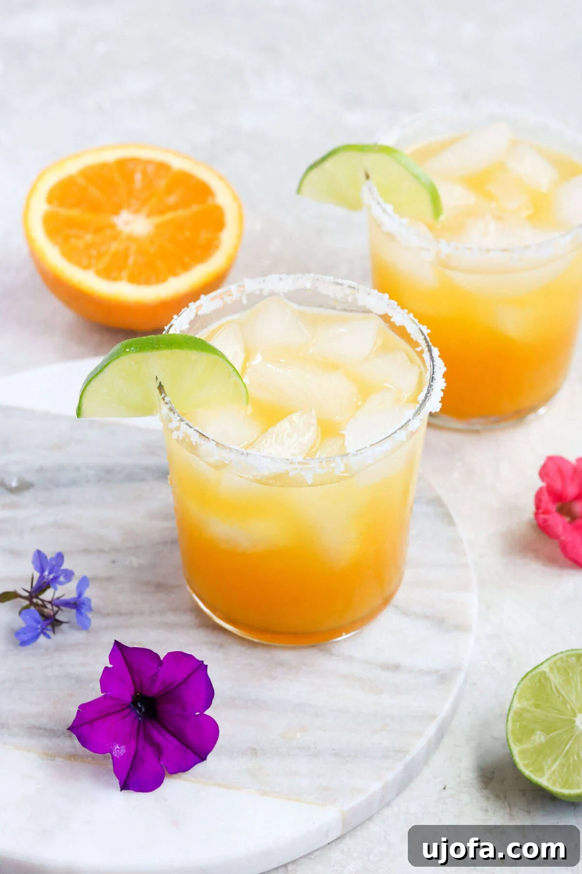 Exotic Passion Fruit Margarita Bliss 2 Two clear glasses filled with vibrant passion fruit margaritas, garnished with lime slices and tropical flowers, sitting next to a half orange.