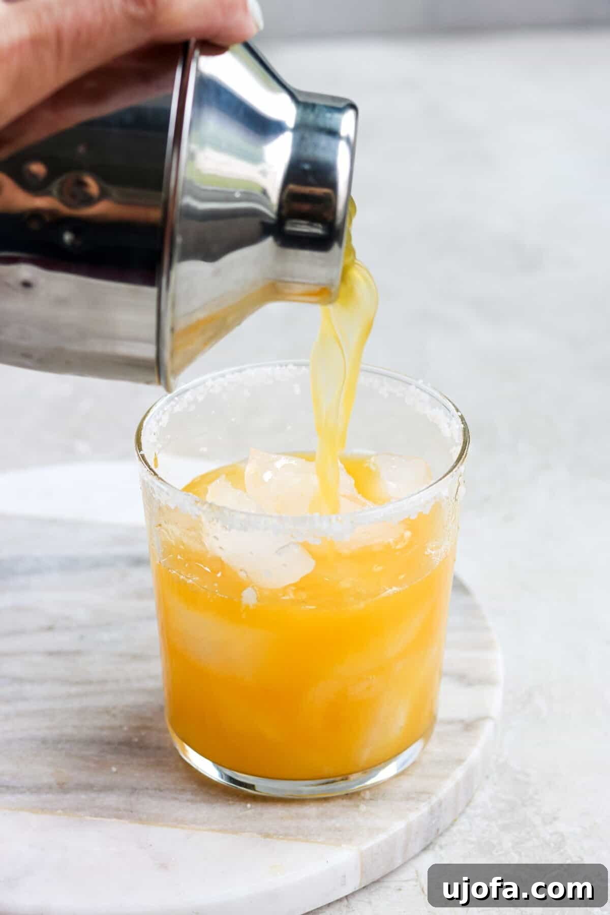 Exotic Passion Fruit Margarita Bliss 5 A cocktail shaker expertly pouring a bright orange passion fruit margarita into a glass with a salted rim and ice.