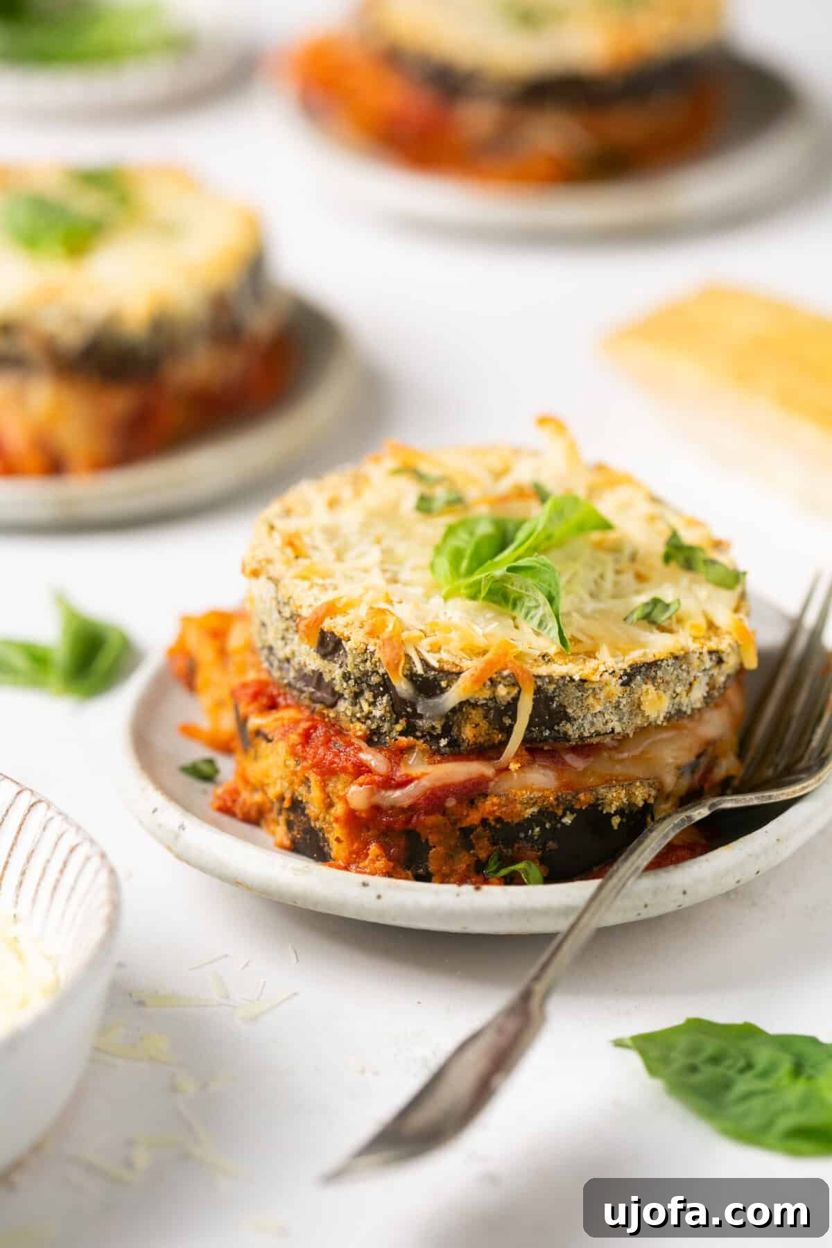 3 individual servings of keto eggplant parmesan on white plates with a silver fork