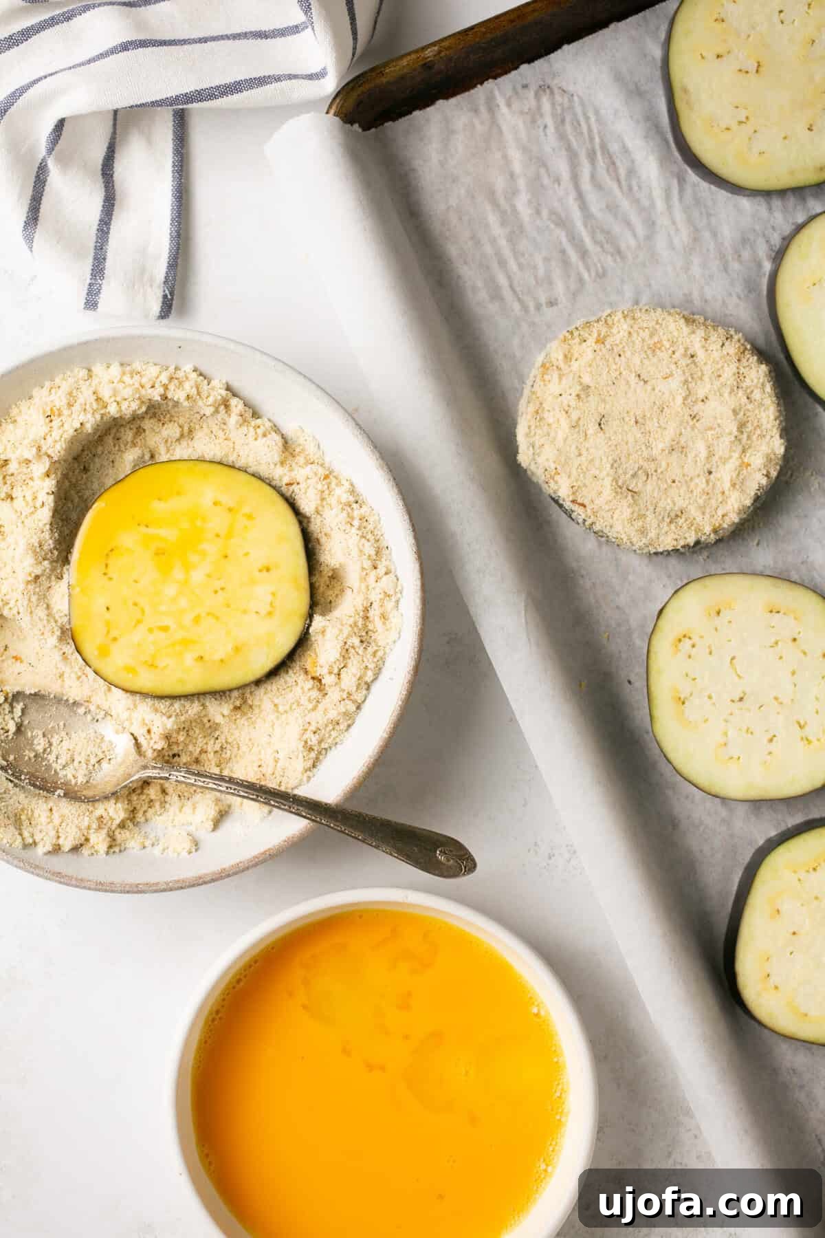 dipping eggplant rounds in egg wash and then an almond flour mixture and placing them on a sheet pan
