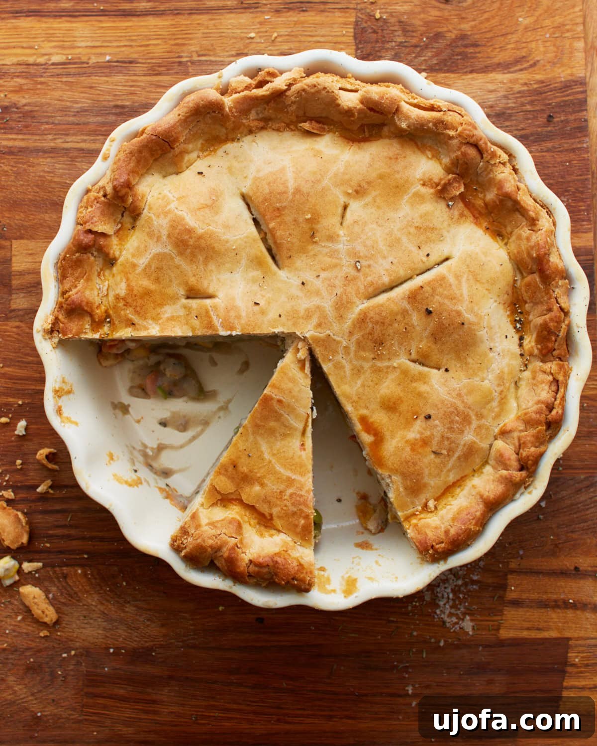The Ultimate Gluten-Free Chicken Pot Pie 2 overhead view of a gluten-free chicken pot pie in a white pie pan on a wooden countertop with 2 slices gone and another slice cut