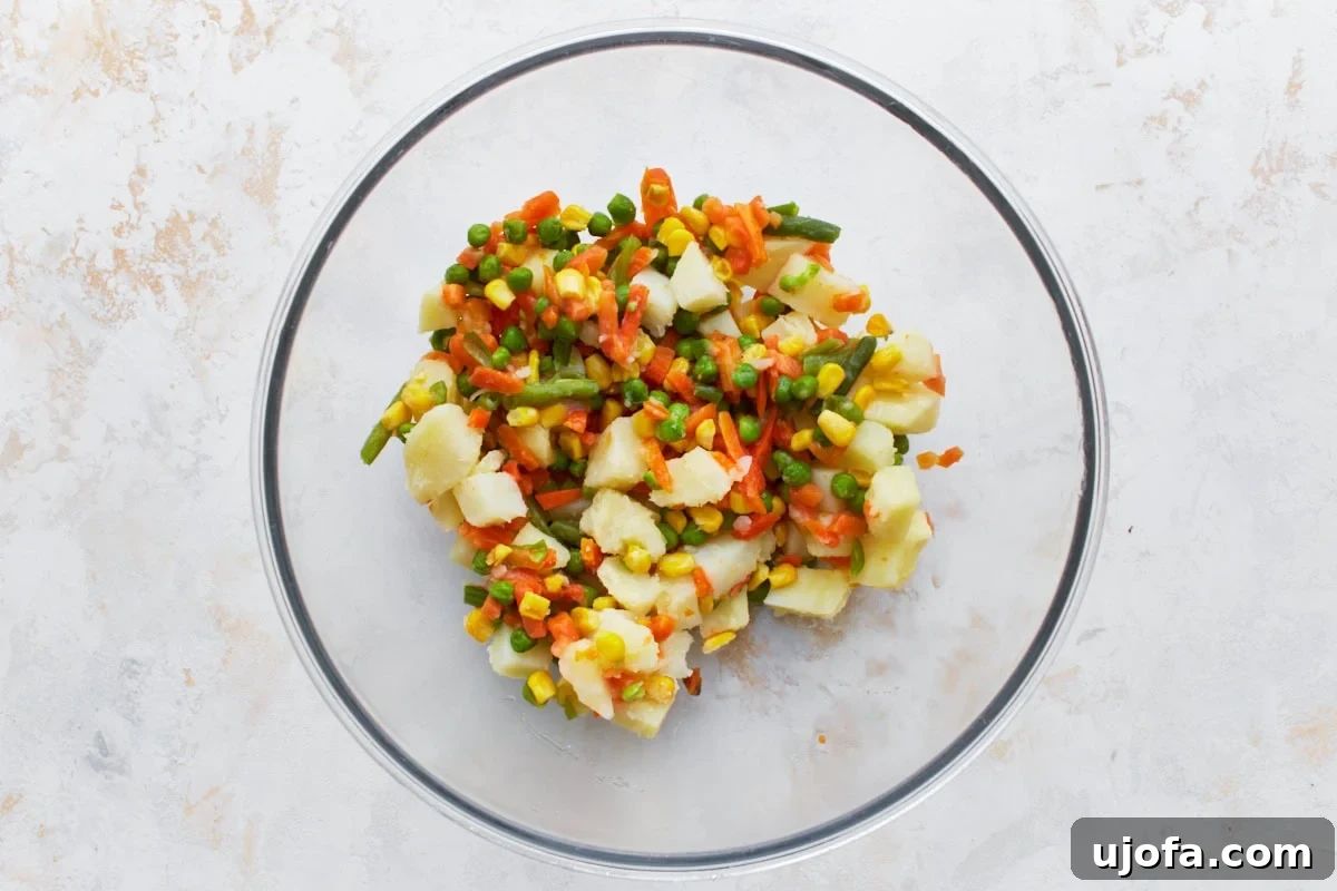 The Ultimate Gluten-Free Chicken Pot Pie 9 mixed vegetables: corn, green beans, carrots, peas, and cubed potatoes in a glass bowl on a light countertop