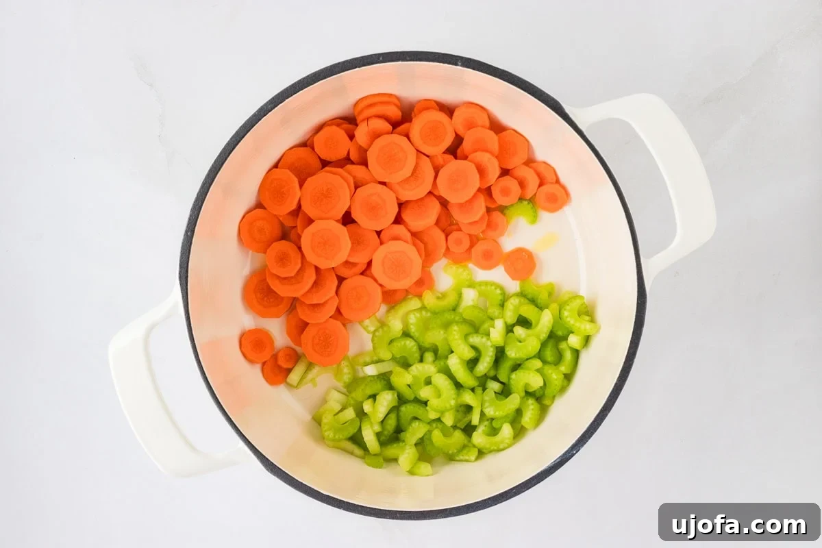 A white pot on a stovetop, filled with neatly sliced raw carrots and celery, ready to be sautéed. The background is light and clean, emphasizing the fresh ingredients.