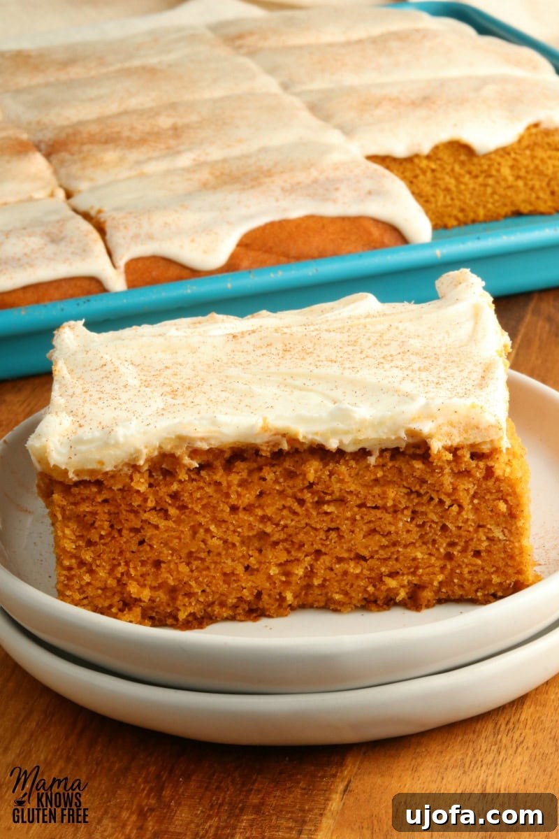 Decadent Gluten-Free Pumpkin Spice Squares 2 A slice of gluten-free pumpkin bar with a generous swirl of cream cheese frosting, elegantly placed on a white plate. In the soft-focus background, a baking pan filled with more delicious bars is visible, suggesting an abundance of this seasonal treat.