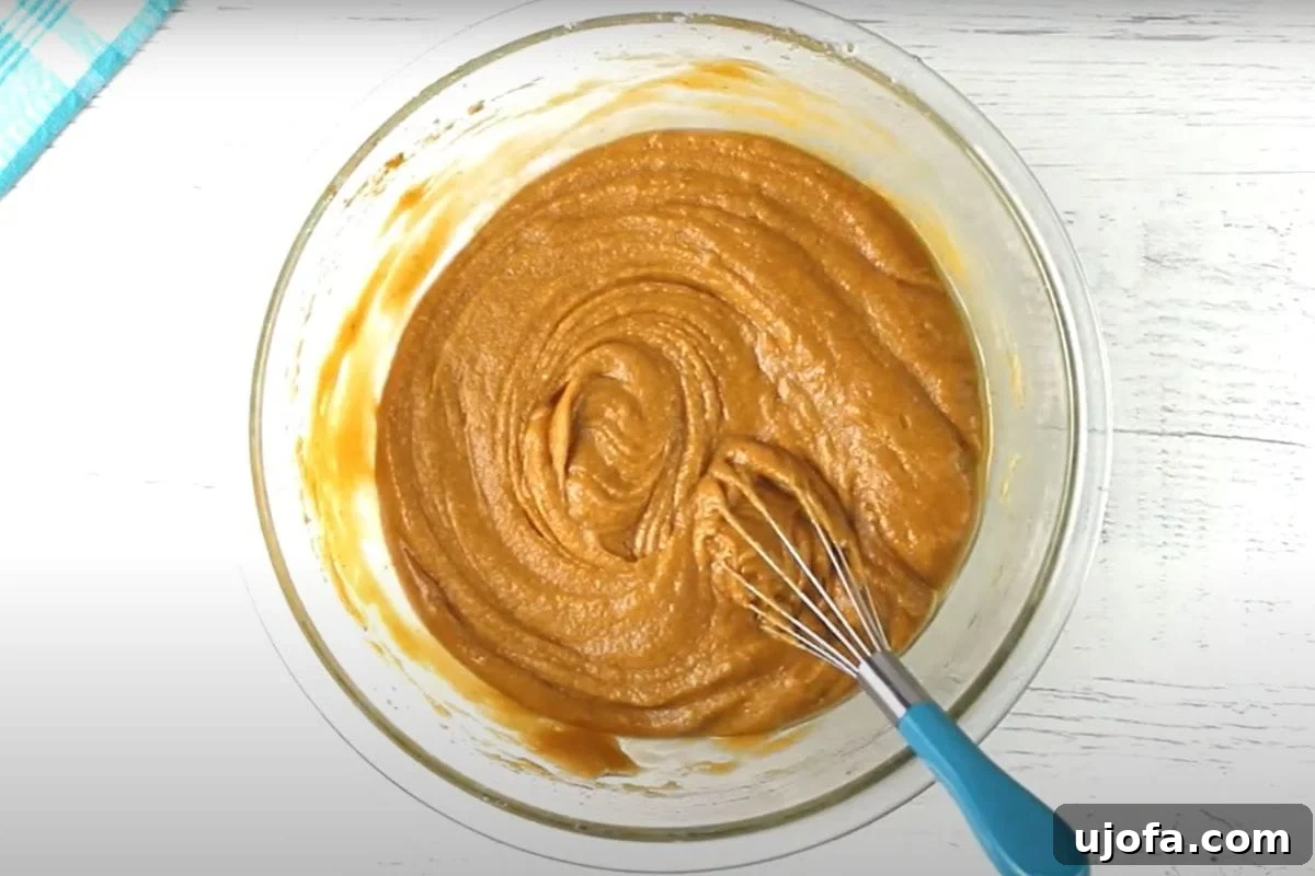 Decadent Gluten-Free Pumpkin Spice Squares 10 Golden vegetable oil is being poured into the thick, spiced pumpkin bar batter in a glass mixing bowl. The oil will be blended in to create a rich, incredibly moist and tender dough for baking.