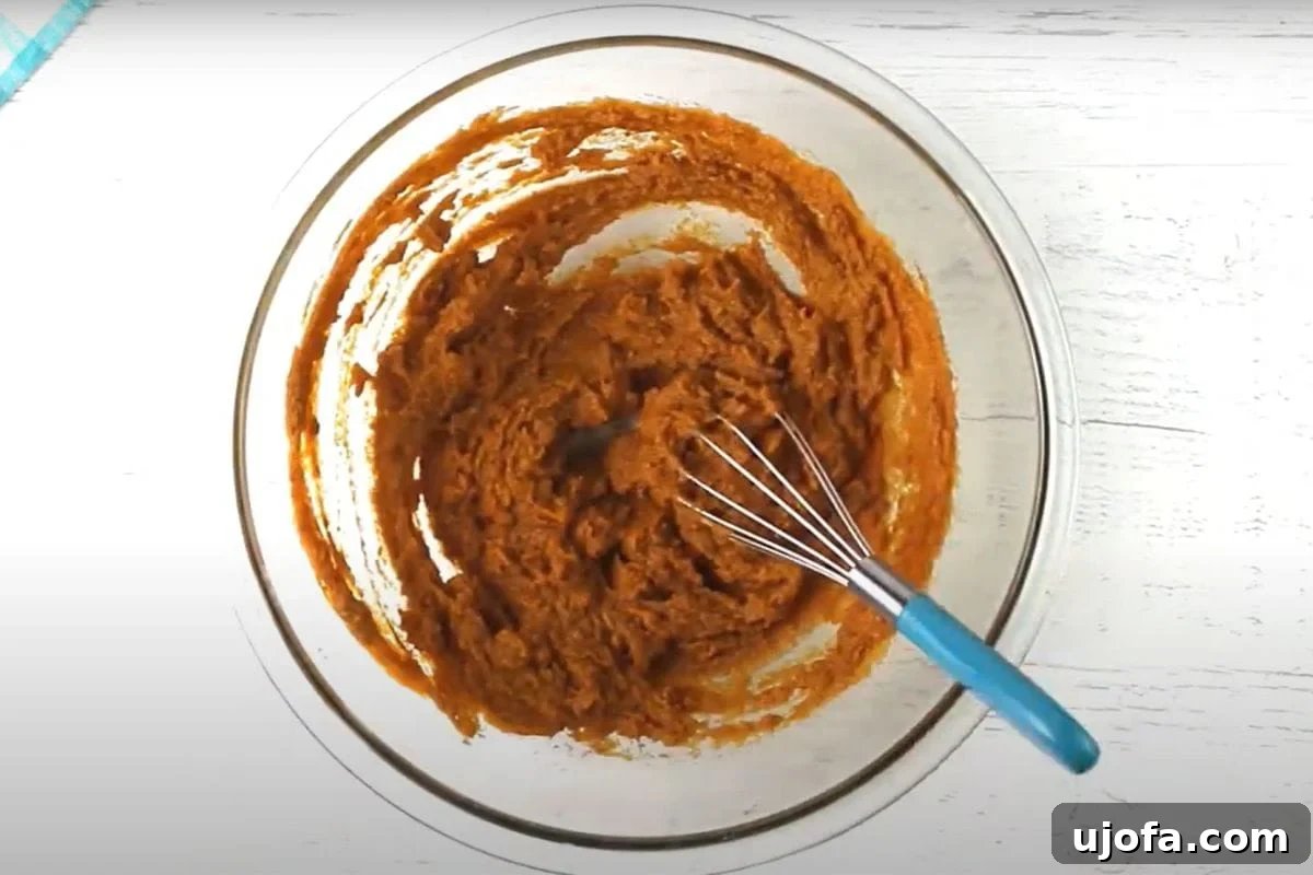 Decadent Gluten-Free Pumpkin Spice Squares 6 Pumpkin puree mixed with a vibrant array of spices including baking powder, baking soda, salt, cinnamon, and pumpkin pie spice, all swirling together in a clear glass mixing bowl, ready for the next ingredients.