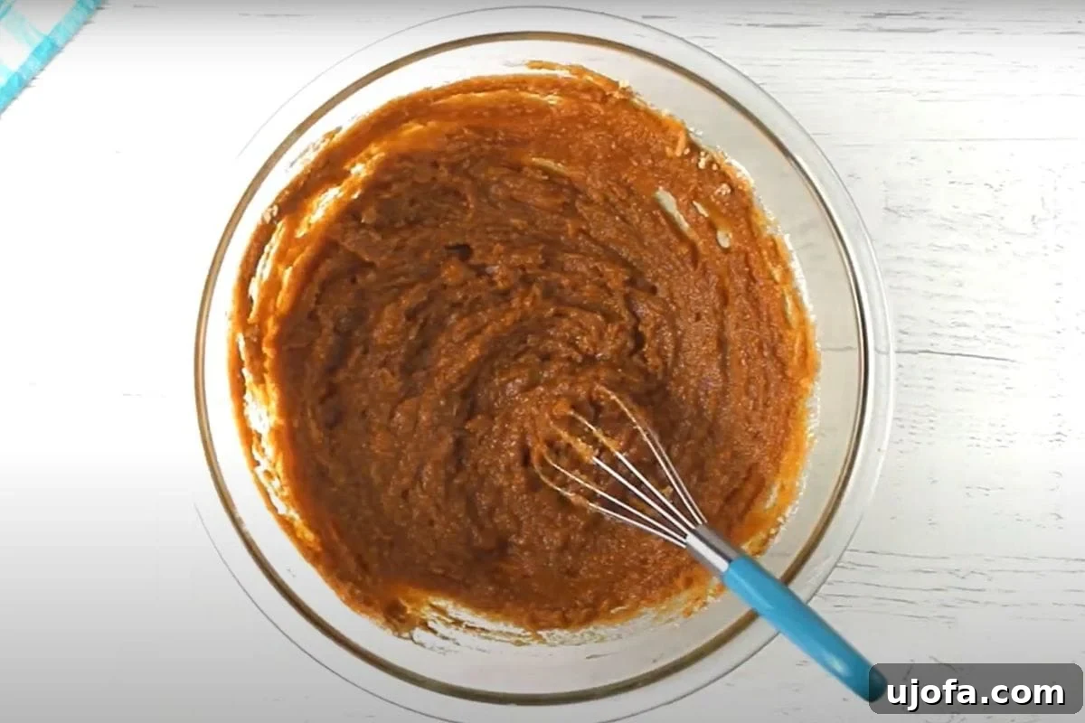 Decadent Gluten-Free Pumpkin Spice Squares 7 Granulated sugar and brown sugar are added to the rich pumpkin and spice mixture in a glass bowl. The mixture starts to transform, becoming smoother and more cohesive, indicating the sugars are dissolving into the wet ingredients.