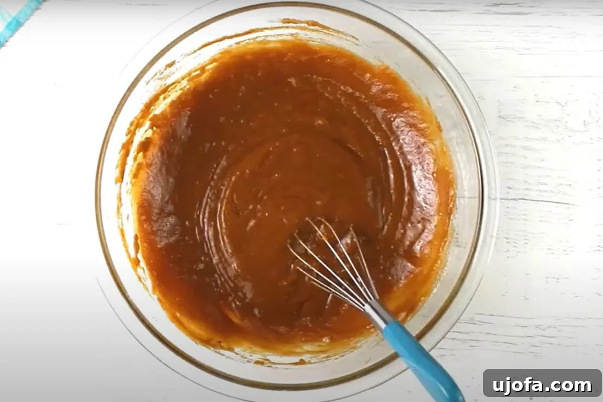 Decadent Gluten-Free Pumpkin Spice Squares 8 Three large eggs have just been cracked into the pumpkin and sugar mixture in a glass mixing bowl. The vibrant yellow yolks stand out against the orange batter, ready to be whisked in and create a cohesive, richer dough.
