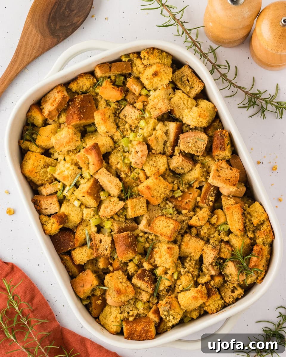 Savory Gluten-Free Cornbread Dressing 2 A baked dish of golden-brown gluten-free cornbread stuffing with herbs, served in a white casserole dish with a wooden spoon and fresh rosemary nearby.