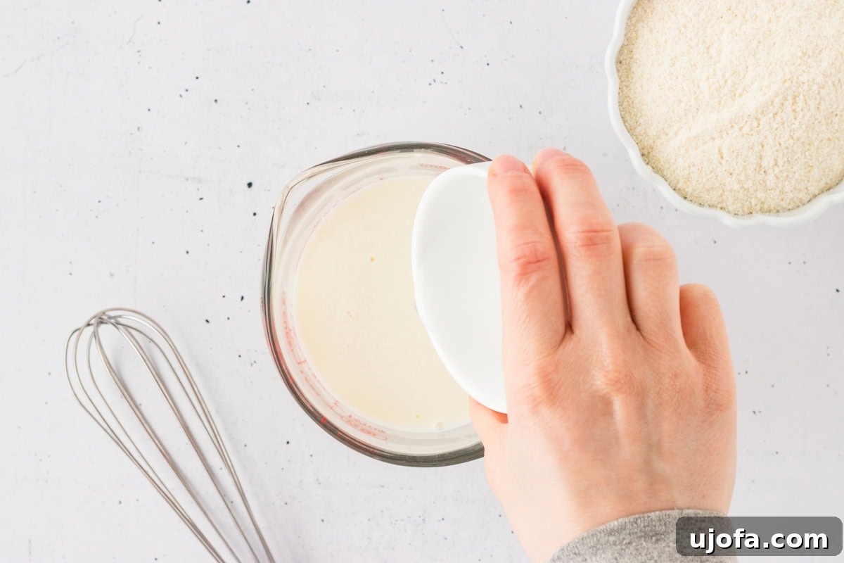 Savory Gluten-Free Cornbread Dressing 5 A hand pouring white vinegar into a measuring cup filled with milk, preparing homemade buttermilk for gluten-free cornbread.