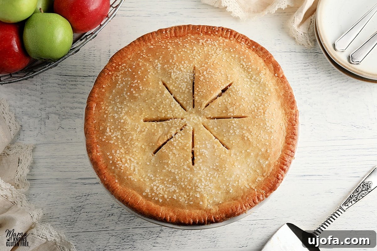 A beautifully baked gluten-free apple pie, perfectly sliced, placed next to a basket of fresh apples and elegant white plates, ready for serving.