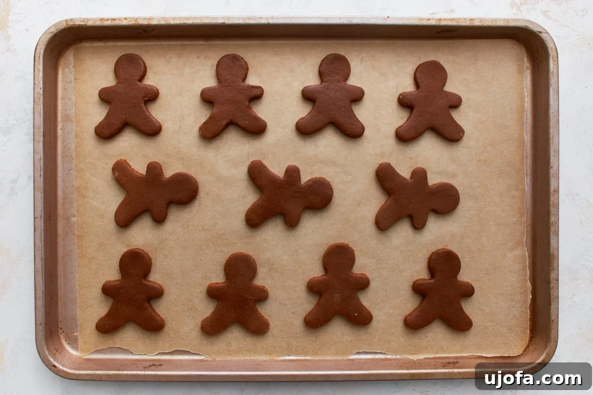 Guilt-Free Gingerbread Bliss 13 A baking sheet lined with parchment paper, holding an arrangement of raw gluten-free gingerbread man cutouts, perfectly spaced and ready for the oven.