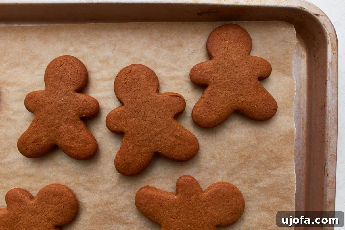 Guilt-Free Gingerbread Bliss 14 A close-up shot of freshly baked gluten-free gingerbread men, golden brown and slightly puffed, cooling on a parchment-lined baking sheet straight out of the oven.