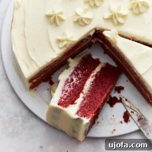 Gluten-free red velvet cake with cream cheese frosting, decorated with piped flowers, and a slice partially removed