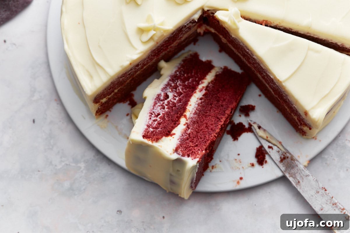 Closeup of gluten-free red velvet cake with cream cheese frosting, decorated with piped flowers, and a slice partially removed