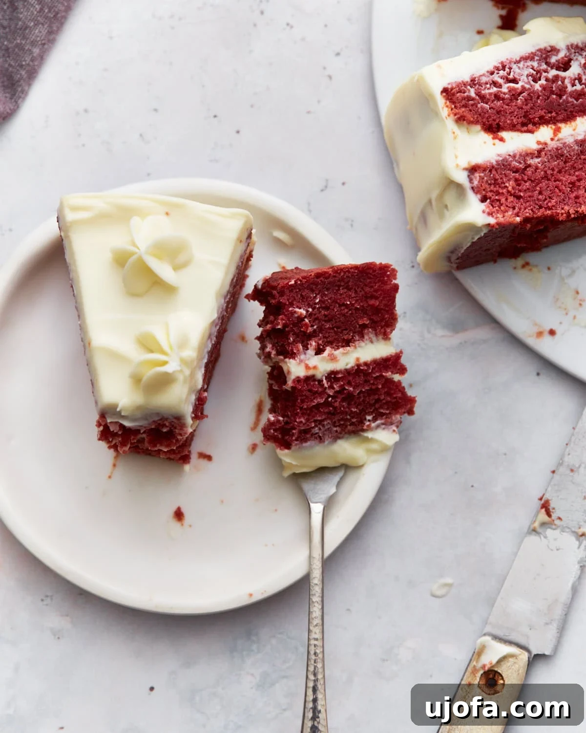 A single slice of gluten-free red velvet cake on a plate, with a fork holding a bite, showing the layers of cream cheese frosting and moist cake.
