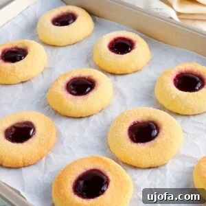 A tempting array of gluten-free thumbprint cookies, each with a vibrant jam filling, cooling on a baking sheet.