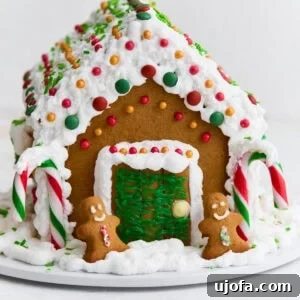 A beautifully assembled gluten-free gingerbread house, adorned with white royal icing, vibrant candies, and two small gingerbread figures at the entrance.