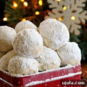 A collection of delicate gluten-free snowball cookies, lightly dusted with powdered sugar, nestled in a vibrant red cookie tin with festive snowflake decor and a twinkling tree in the background.