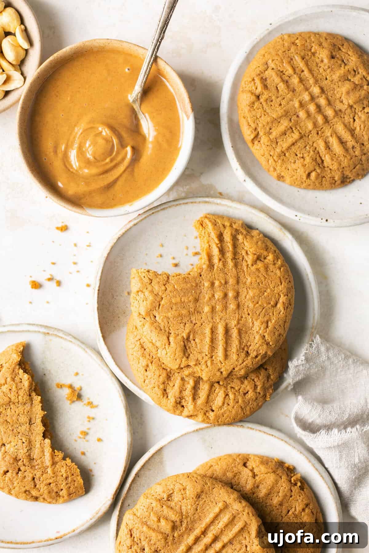 Freshly baked gluten-free peanut butter cookies artfully arranged on small white plates, accompanied by a bowl of creamy peanut butter and a crisp white napkin.