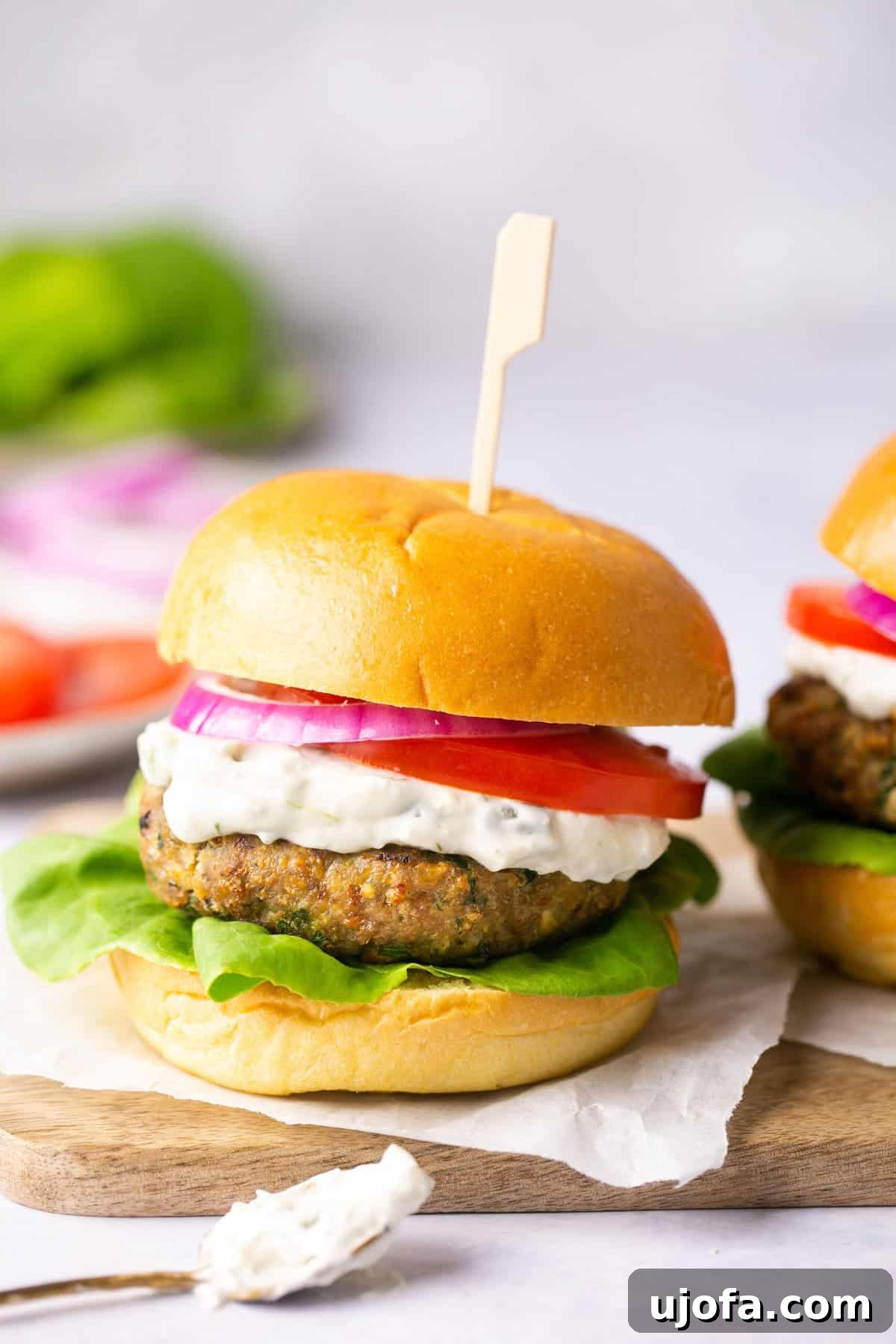 A perfectly cooked turkey burger on a gluten-free bun, generously topped with creamy tzatziki sauce, fresh tomato slices, crisp lettuce, and vibrant red onion, ready to be enjoyed.