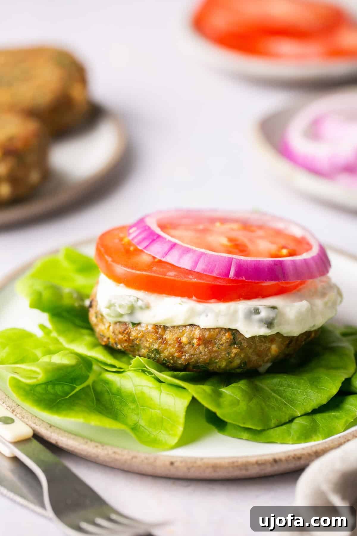 A beautifully presented air-fried turkey burger, resting on a crisp lettuce leaf and topped with fresh tomato, red onion, and a generous drizzle of creamy tzatziki sauce, highlighting a healthy and delicious meal.