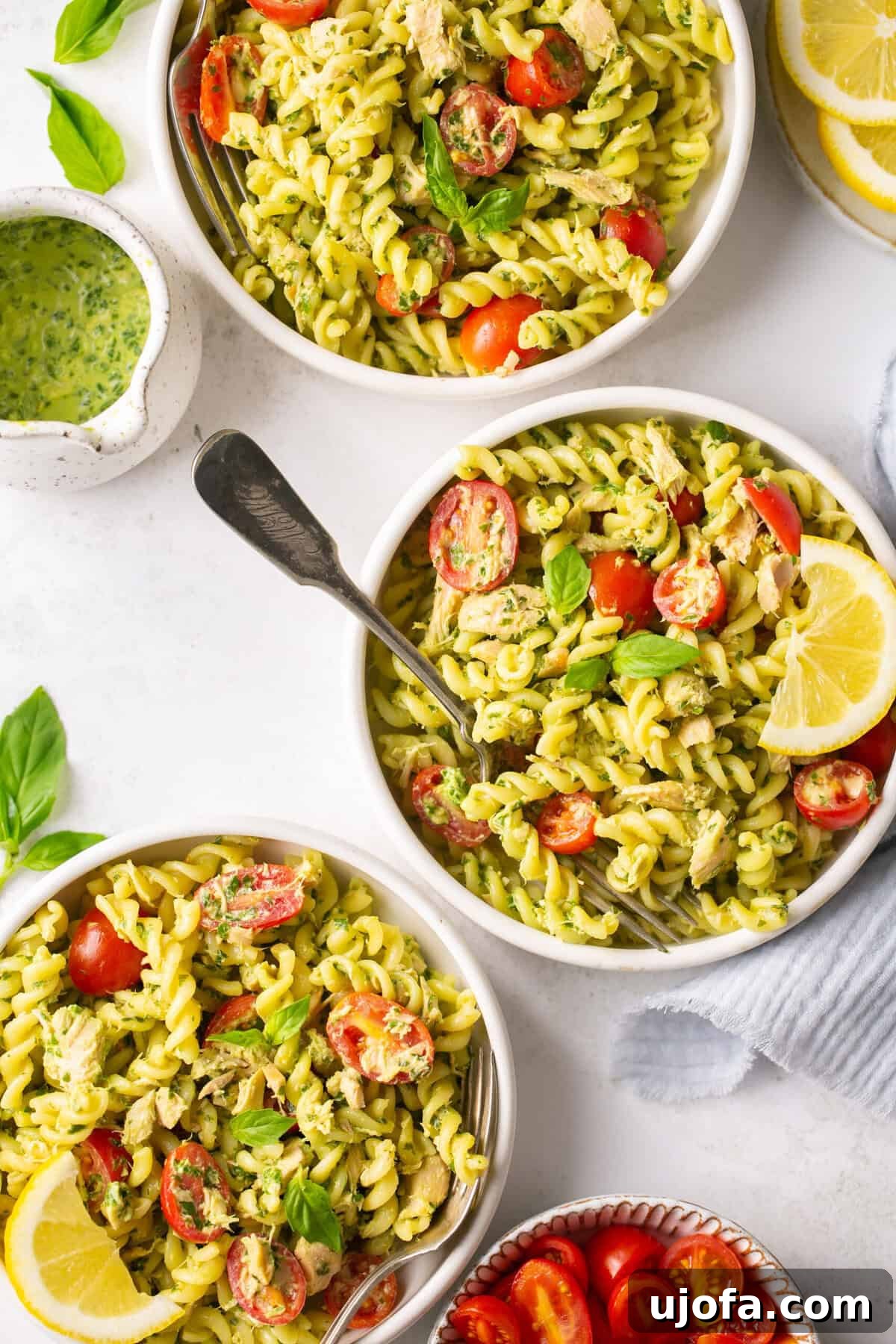 Effortless Gluten-Free Tuna Pesto Pasta 2 three white bowls of pesto tuna pasta with tomatoes next to a saucer with homemade pesto sauce