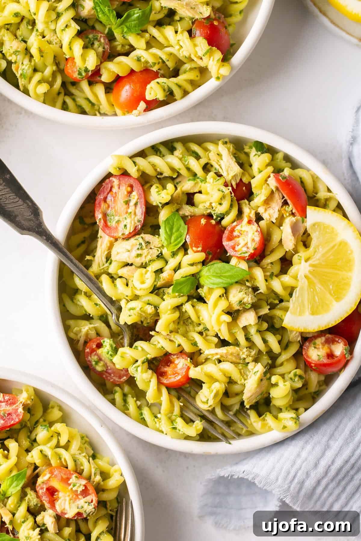 Effortless Gluten-Free Tuna Pesto Pasta 5 a closeup shot of three white bowls filled with pesto pasta and tomatoes.