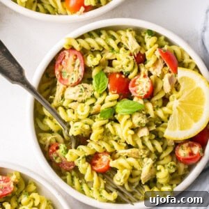 dairy free pesto tuna pasta in a bowl with tomatoes, basil, and a slice of lemon