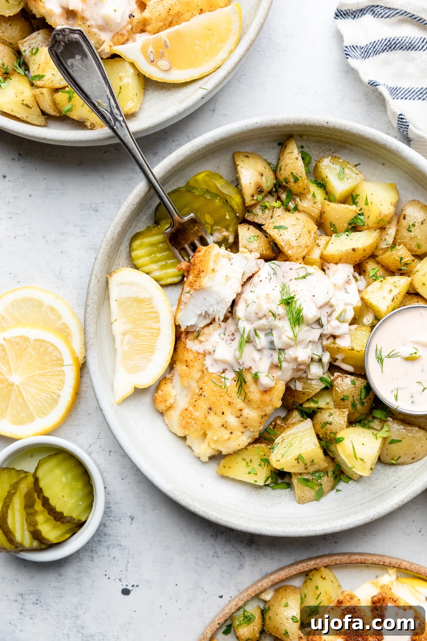 Gluten-Free Fish and Chips served with roasted potatoes, a side of homemade tartar sauce, and garnished with lemon and pickles in a rustic bowl.