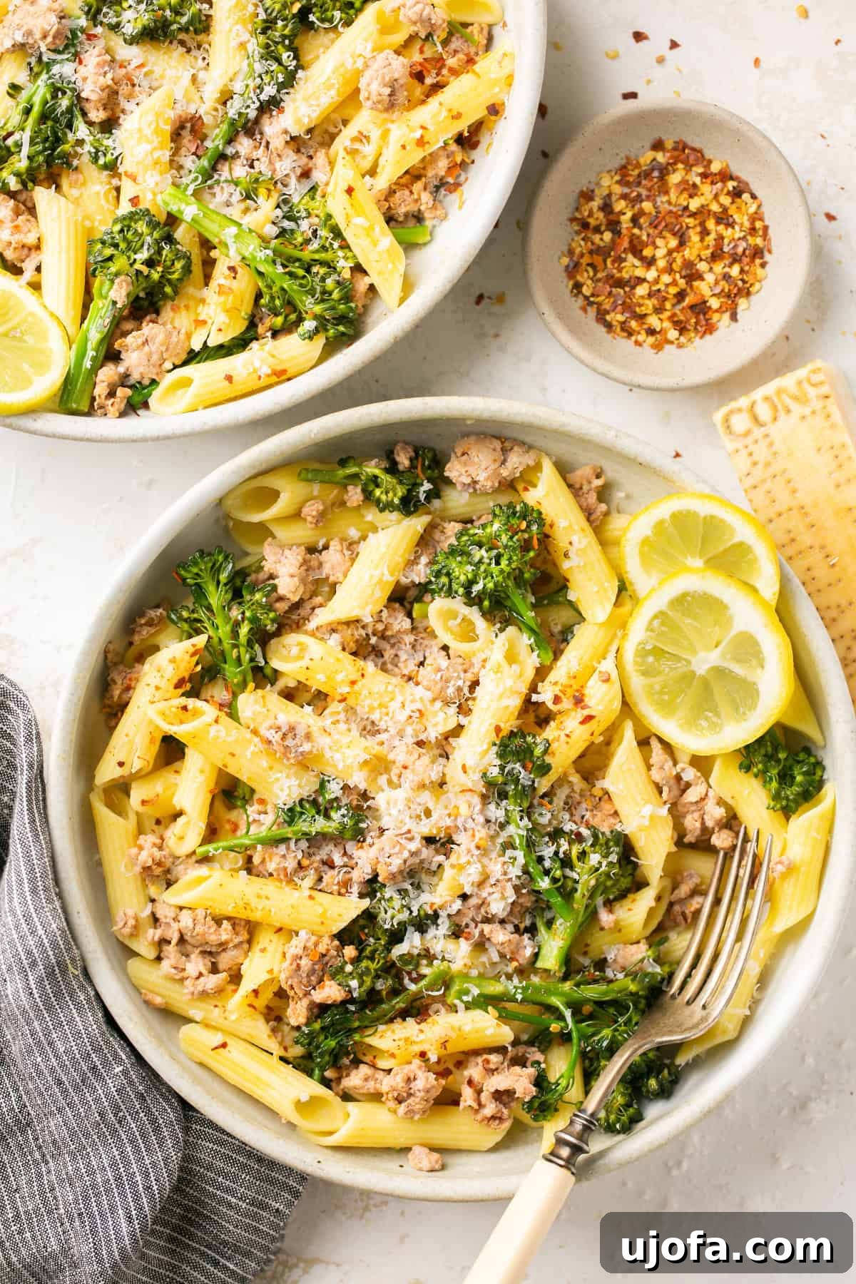 Hearty Sausage and Broccolini Pasta 2 Two white bowls filled with delicious sausage broccolini penne pasta, garnished with crushed red pepper flakes.