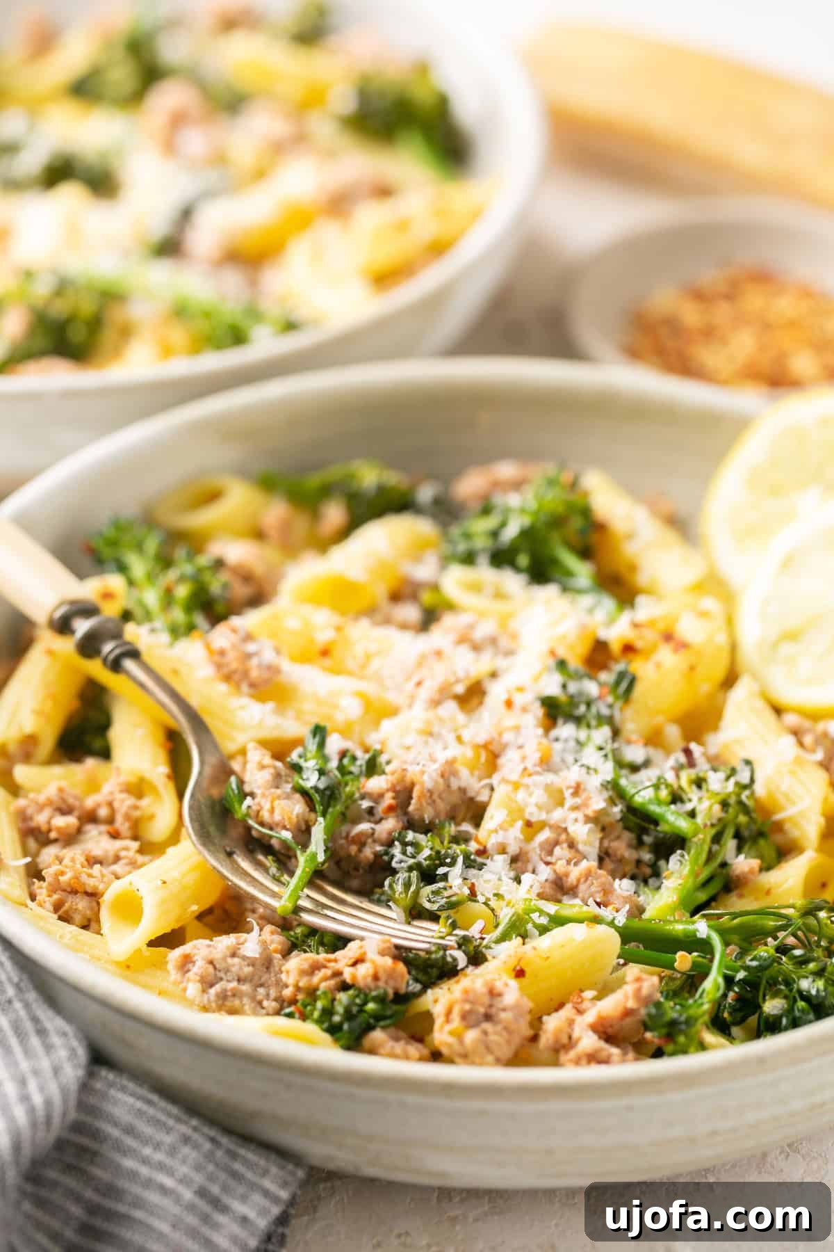 Hearty Sausage and Broccolini Pasta 6 A close-up shot of sausage broccolini pasta in a white bowl, garnished with fresh lemon wedges.