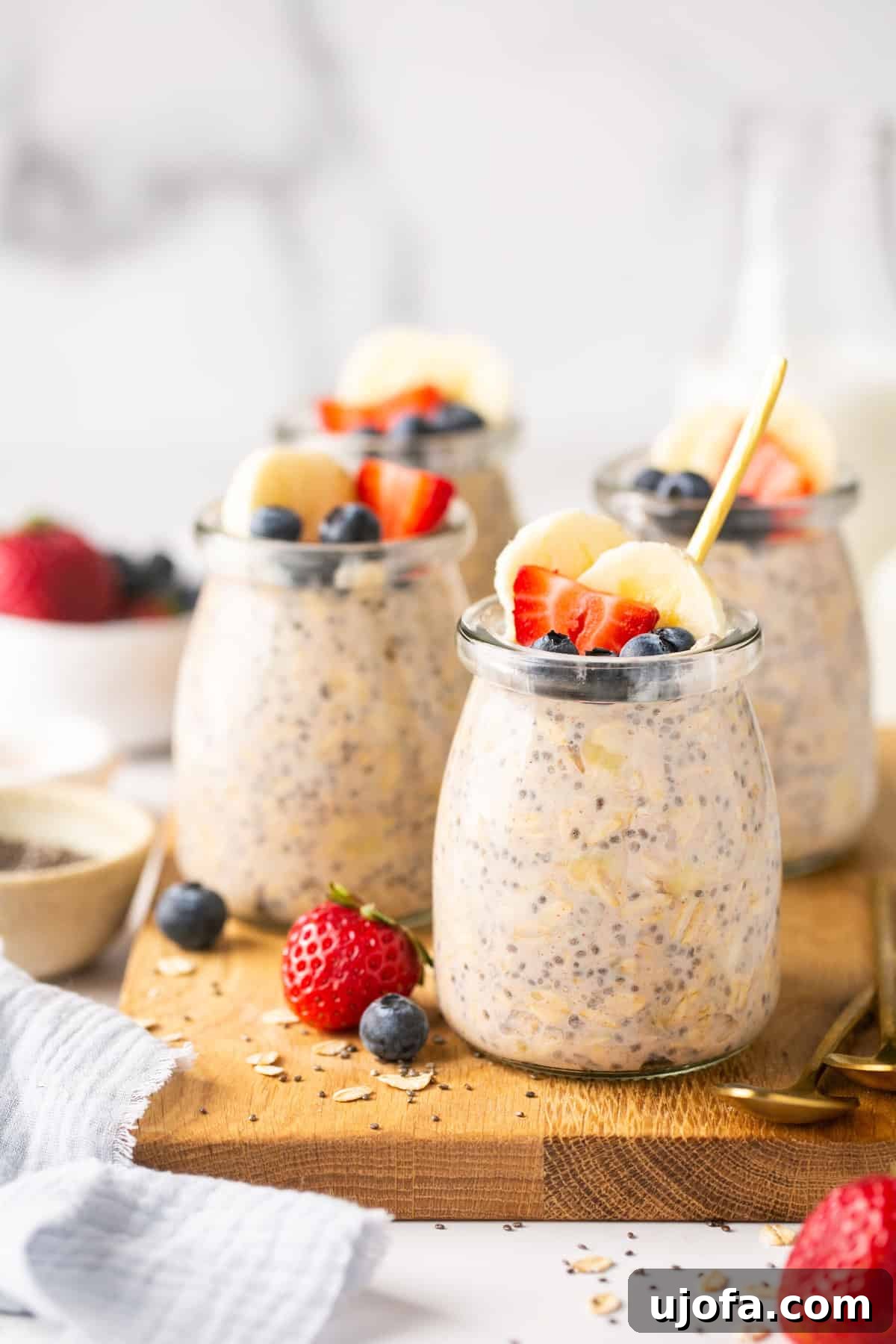 Protein Power Overnight Oats 2 Mini glass jars filled with protein overnight oats, garnished with fresh berries and banana slices, sitting on a rustic wooden cutting board.
