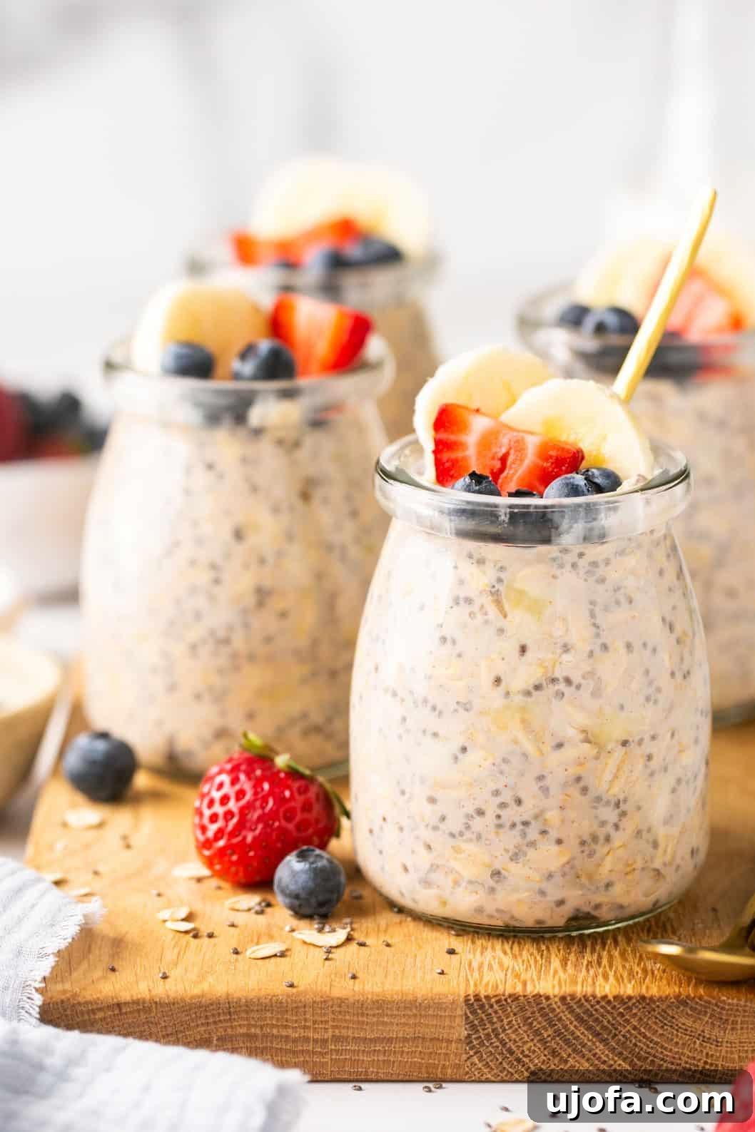 Protein Power Overnight Oats 5 Four small glass jars of protein overnight oats topped with various fresh fruits like berries and bananas, arranged on a wooden board.