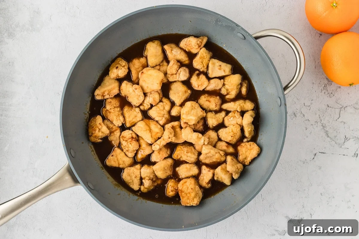 Tangy Gluten-Free Orange Chicken 17 Golden, crispy chicken pieces added to the thickened orange sauce in a skillet, ready to be coated.