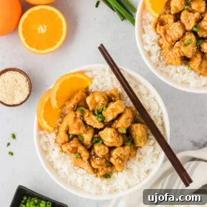 Tangy Gluten-Free Orange Chicken 3 A white bowl filled with gluten-free orange chicken served over white rice, garnished with fresh orange slices, green onions, and sesame seeds. Whole oranges and scallions are displayed in the background for a fresh presentation.