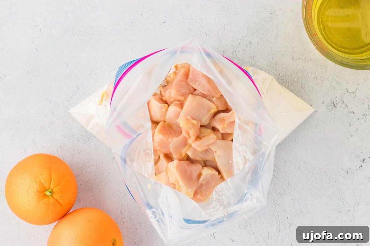 Tangy Gluten-Free Orange Chicken 8 Diced raw chicken placed in a Ziploc bag with gluten-free flour mixture, ready for breading, next to fresh oranges and oil for frying.