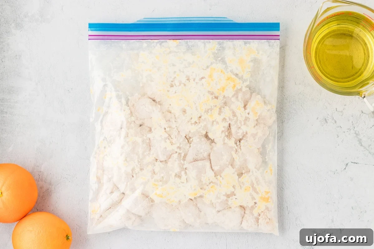 Tangy Gluten-Free Orange Chicken 9 A sealed Ziploc bag filled with breaded raw chicken pieces, coated in a gluten-free flour mixture, with fresh oranges and cooking oil nearby.
