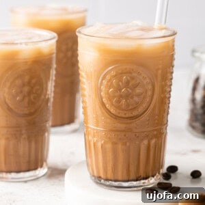 mocha iced coffee in a glass with a straw with coffee beans on the side