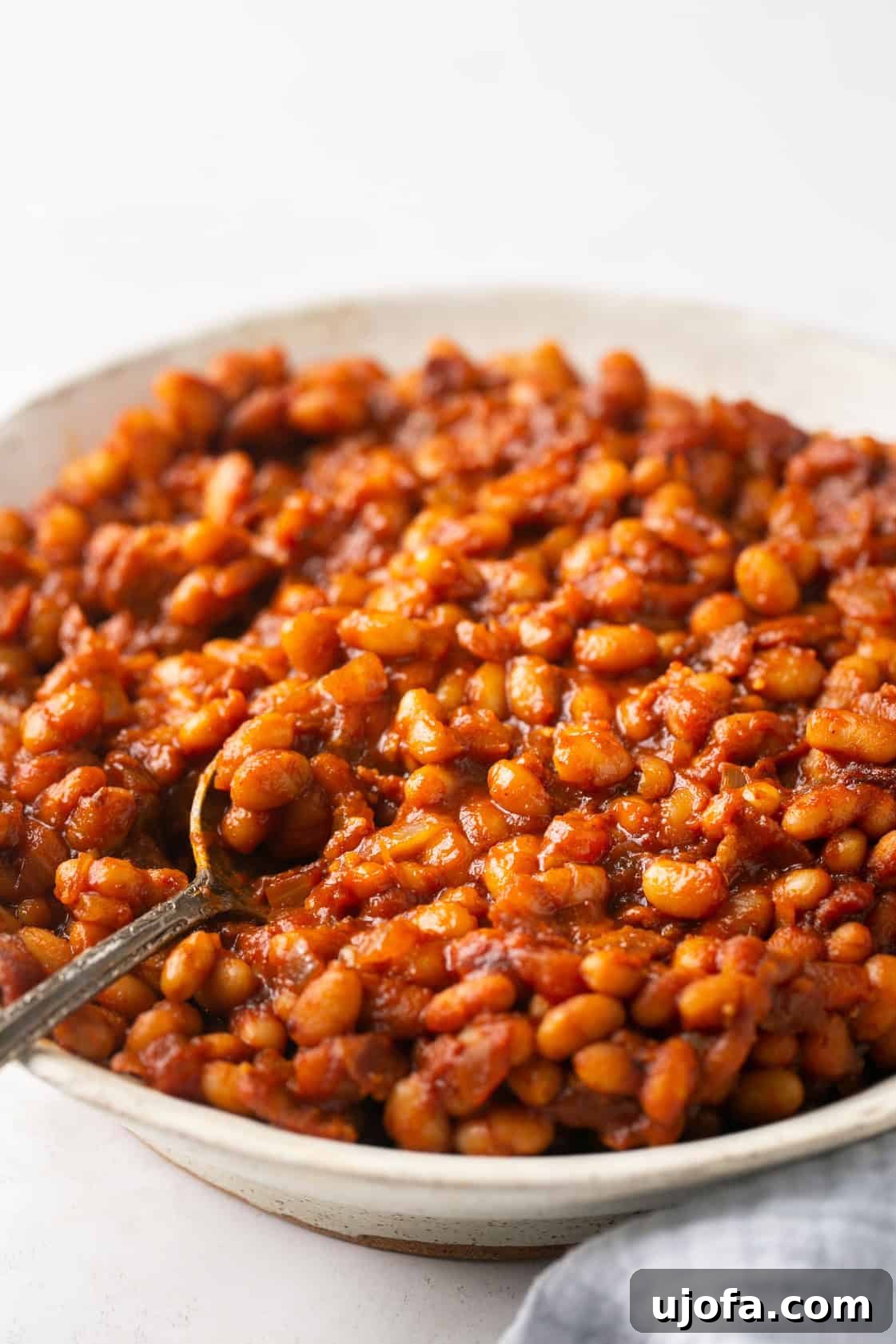 A bowl of healthy baked beans with a silver spoon, ready to be served.