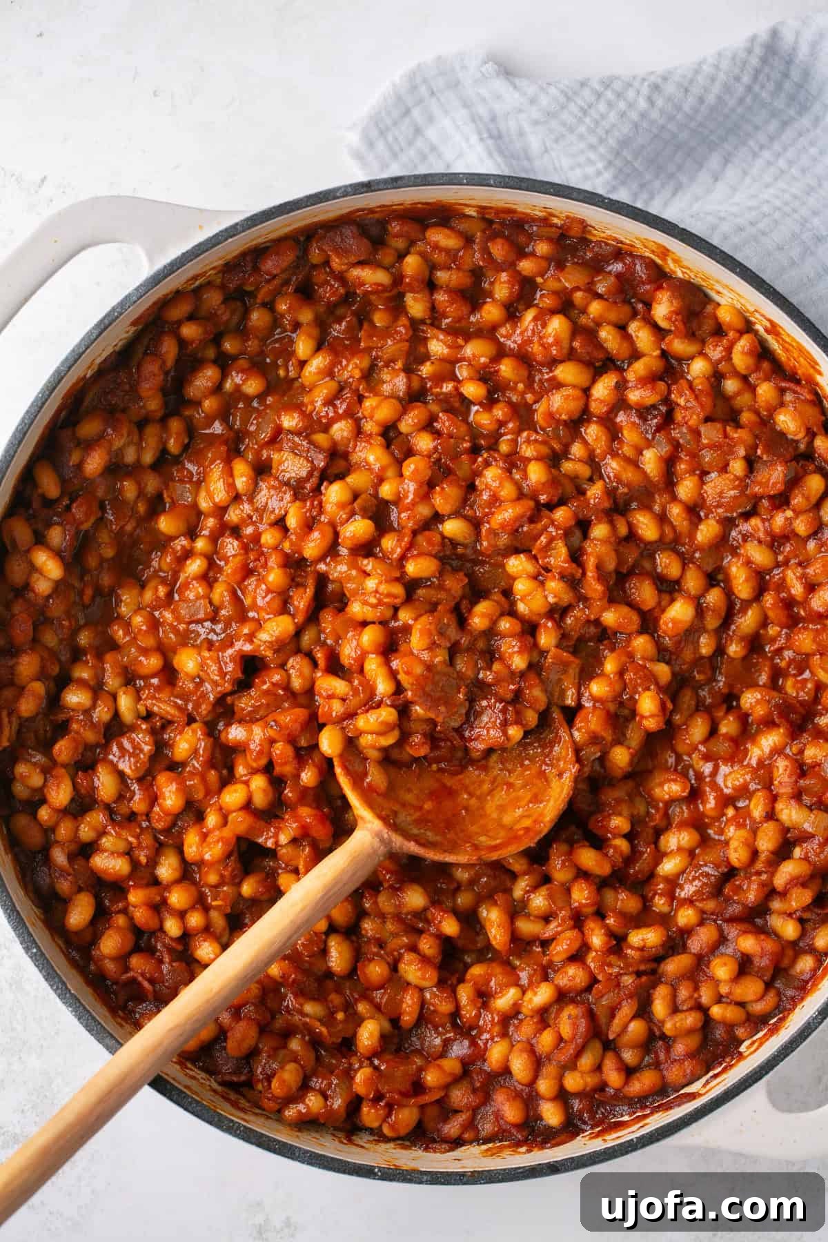 A pot of healthy baked beans simmering on the stovetop, with a wooden spoon resting on the side.