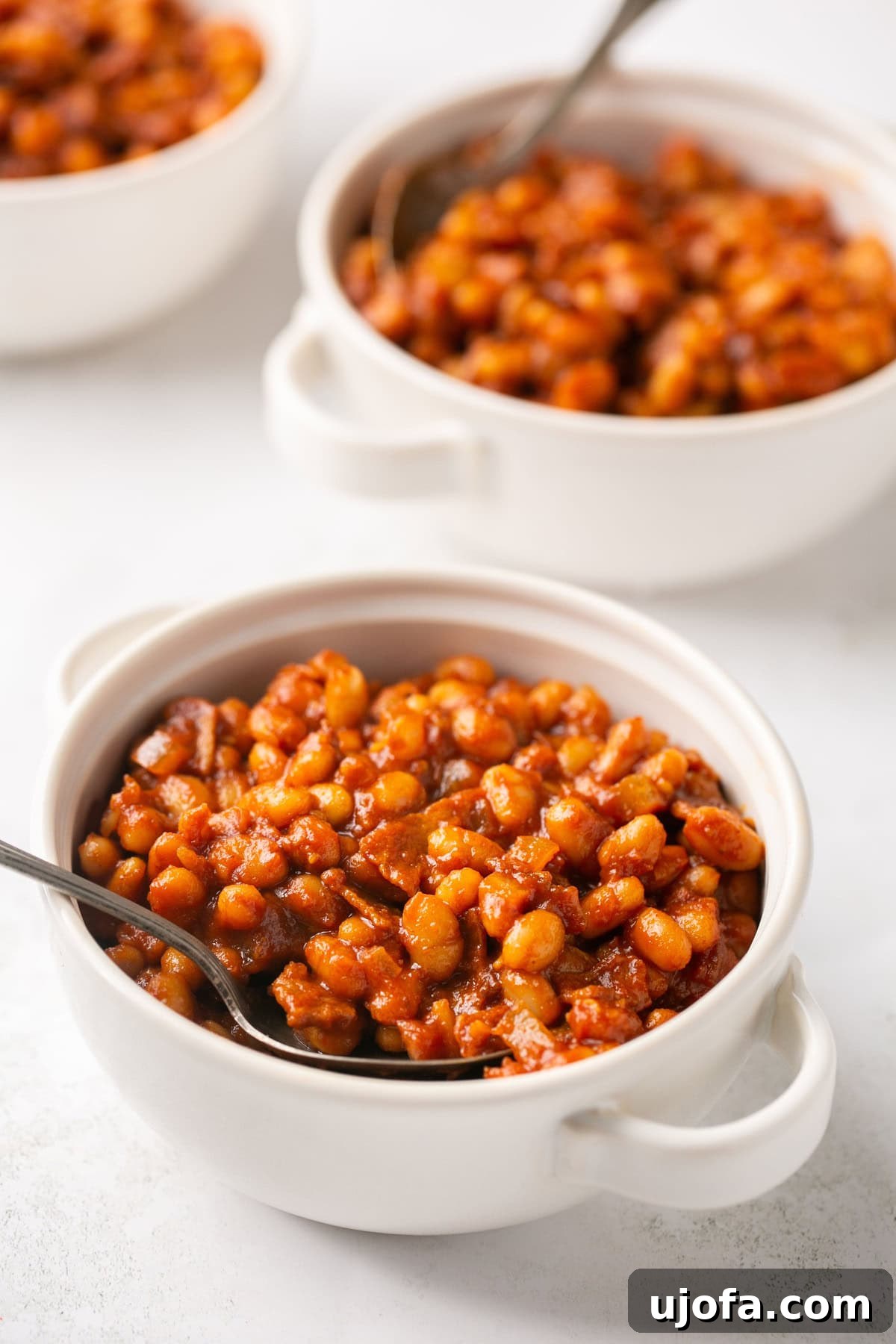 Two small white bowls filled with healthy baked beans, garnished with fresh herbs, and silver spoons.