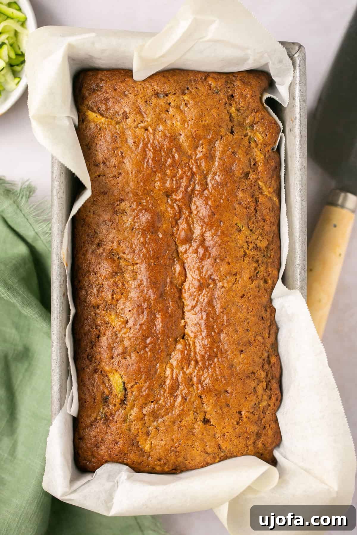 a loaf of gluten free zucchini bread in a metal loaf pan lined with parchment paper