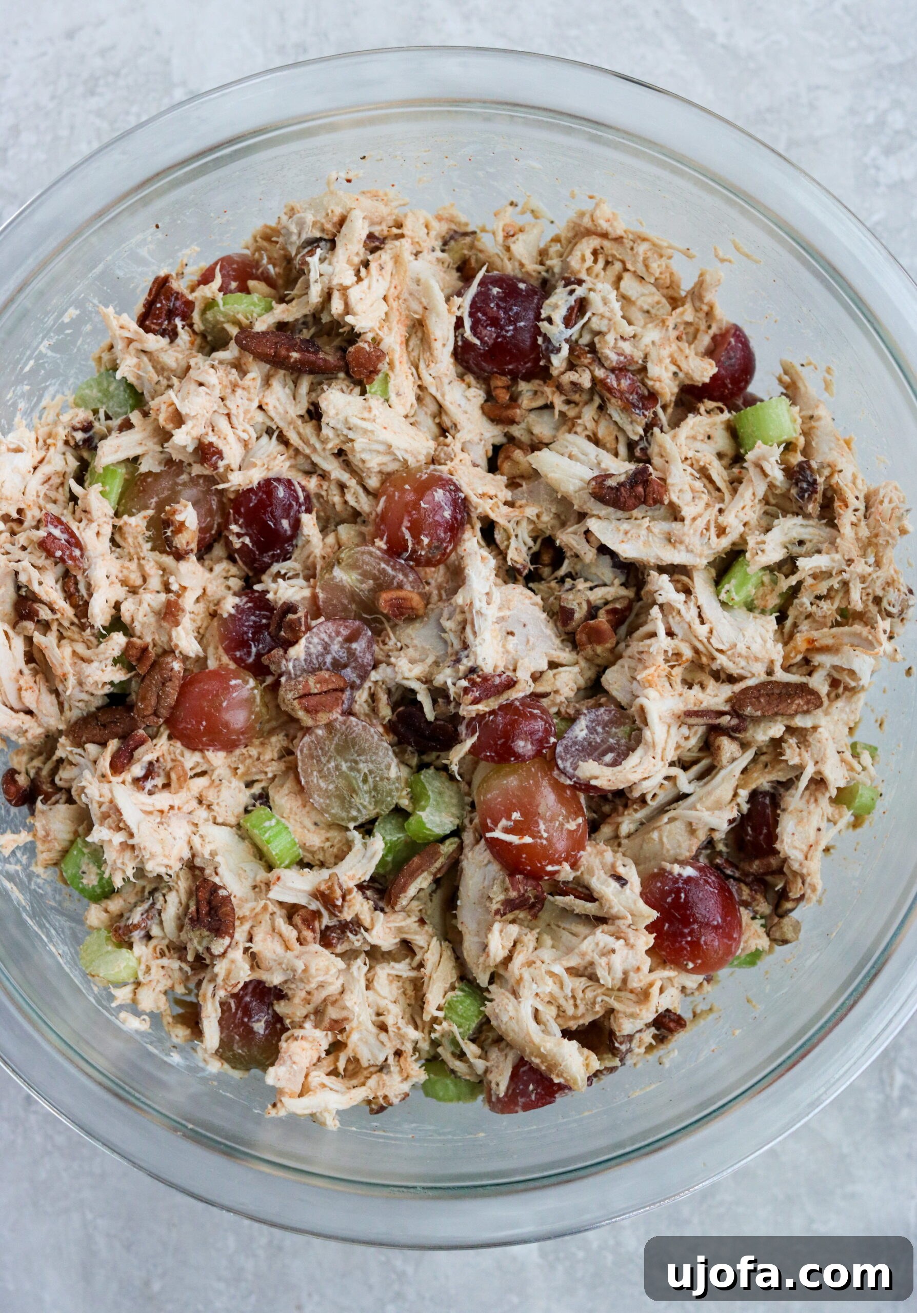 Ingredients in a glass bowl with grapes, pecans, and celery, showcasing the finished chicken salad