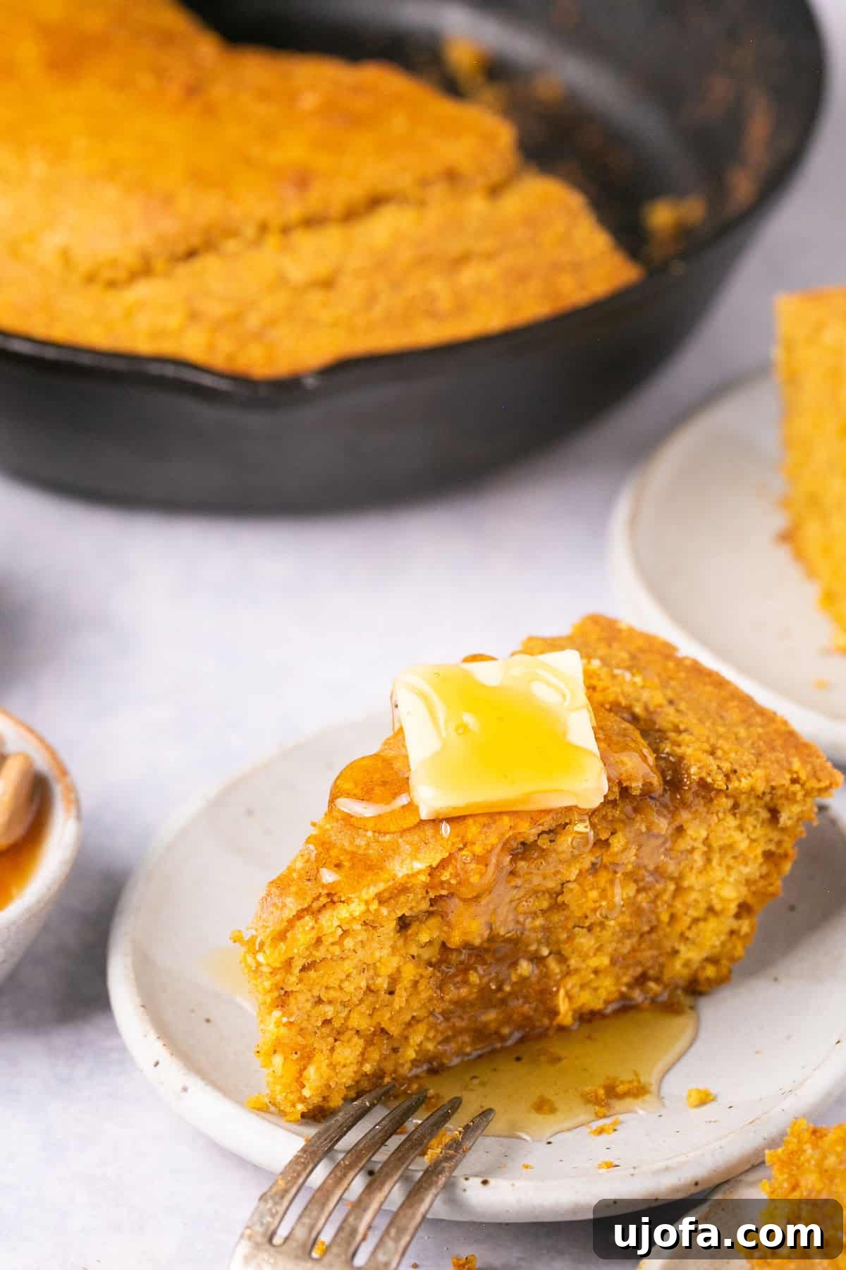 A close-up shot of a single slice of sweet potato cornbread, generously drizzled with golden honey and melted butter, highlighting its tender texture.