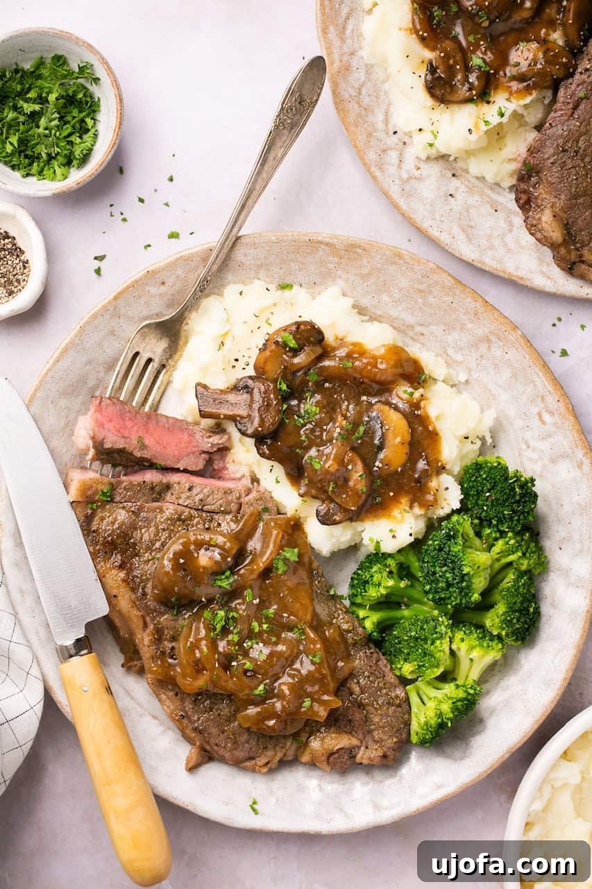 Instant Pot steak served with homemade onion-mushroom gravy, mashed potatoes, and broccoli on a plate with a fork and a steak knife